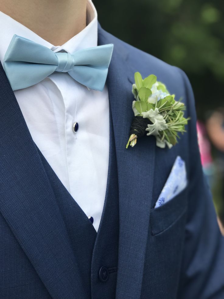 a man wearing a blue suit with a bow tie and flower in his lapel