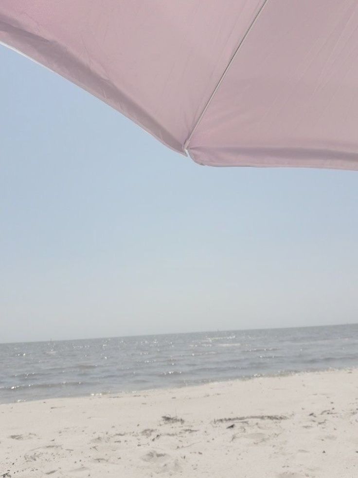 a pink umbrella on the beach with water in the backgrouund and sky in the background