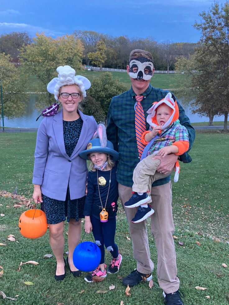 two adults and a child dressed up in halloween costumes standing on grass with pumpkins