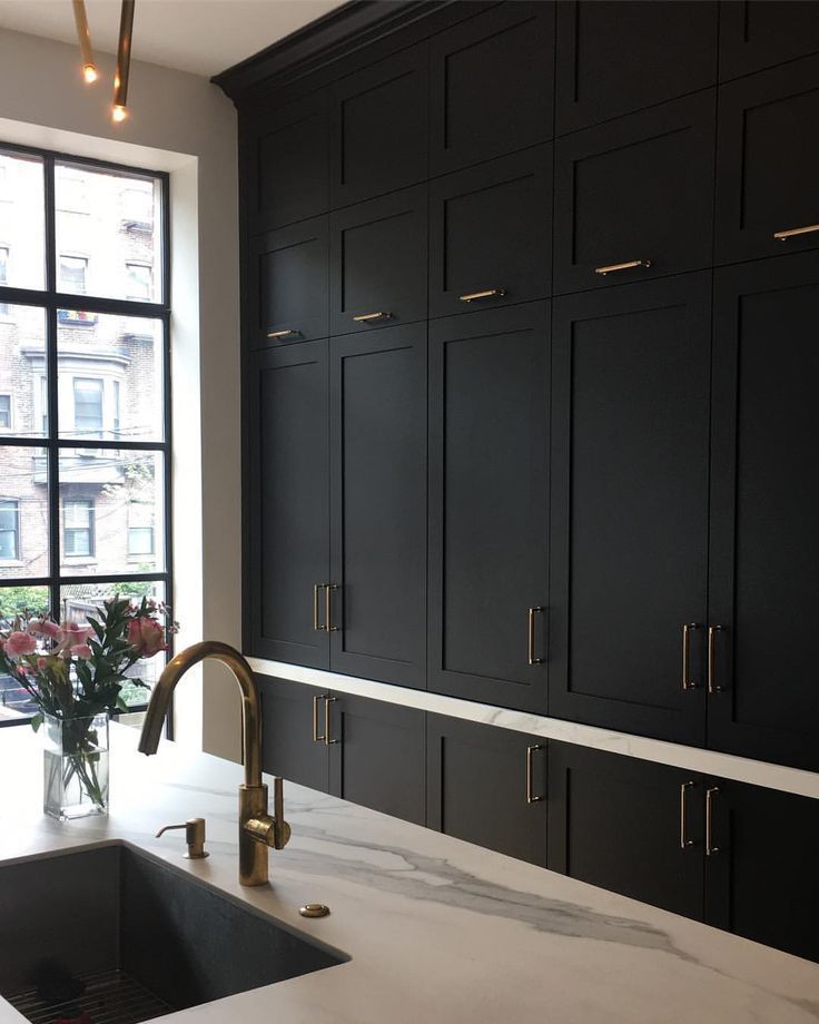 a kitchen with black cabinets and marble counter tops, gold faucet, and a large window