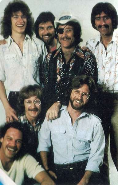 a group of men standing next to each other in front of a white wall smiling