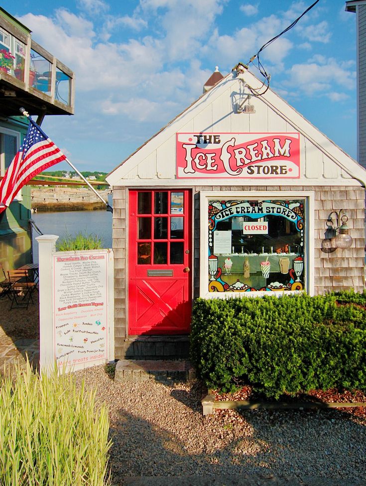 the ice cream store has an american flag on it's display stand next to some bushes