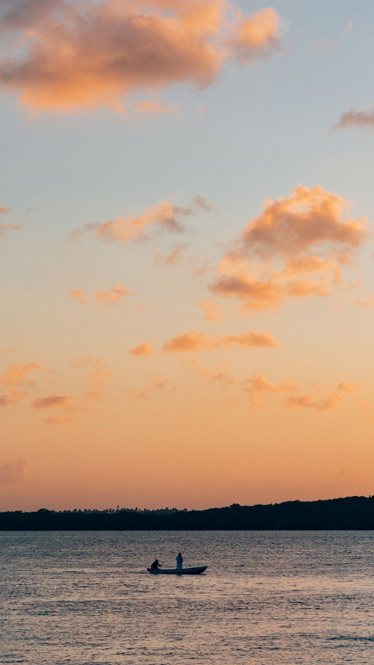 two people in a small boat on the water at sunset or dawn with clouds above them