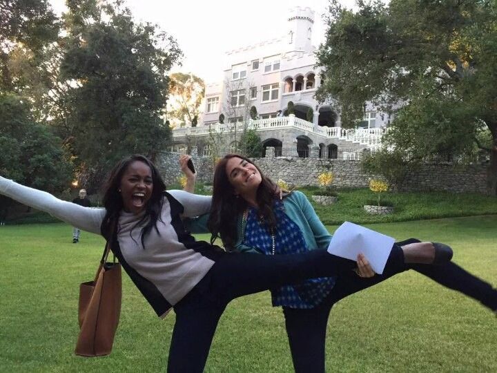 two young women are posing for the camera in front of a large building and trees