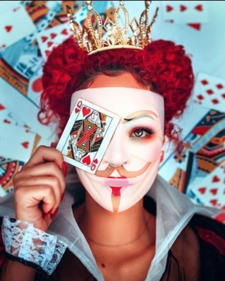 a woman with red hair wearing a white mask and holding playing cards in front of her face