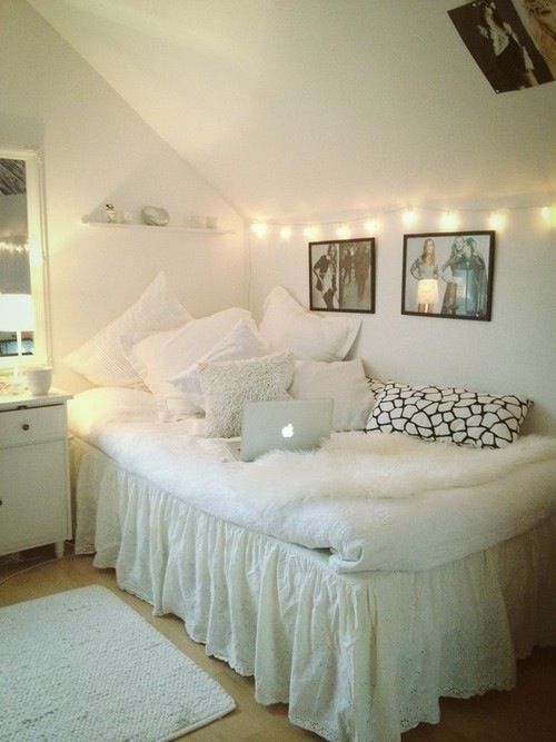 a white bed sitting in a bedroom next to a wall with pictures hanging on it