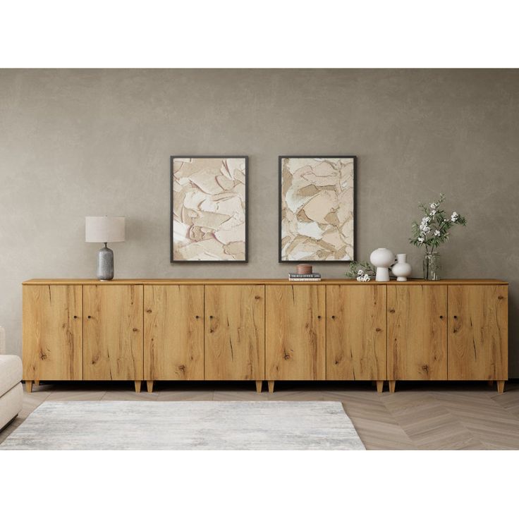 two paintings hang on the wall above a large wooden cabinet in a living room with a white rug