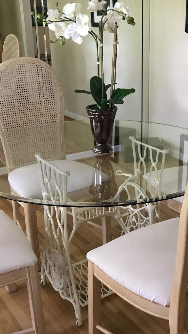 a glass dining table with white chairs and flowers in a vase on the top shelf