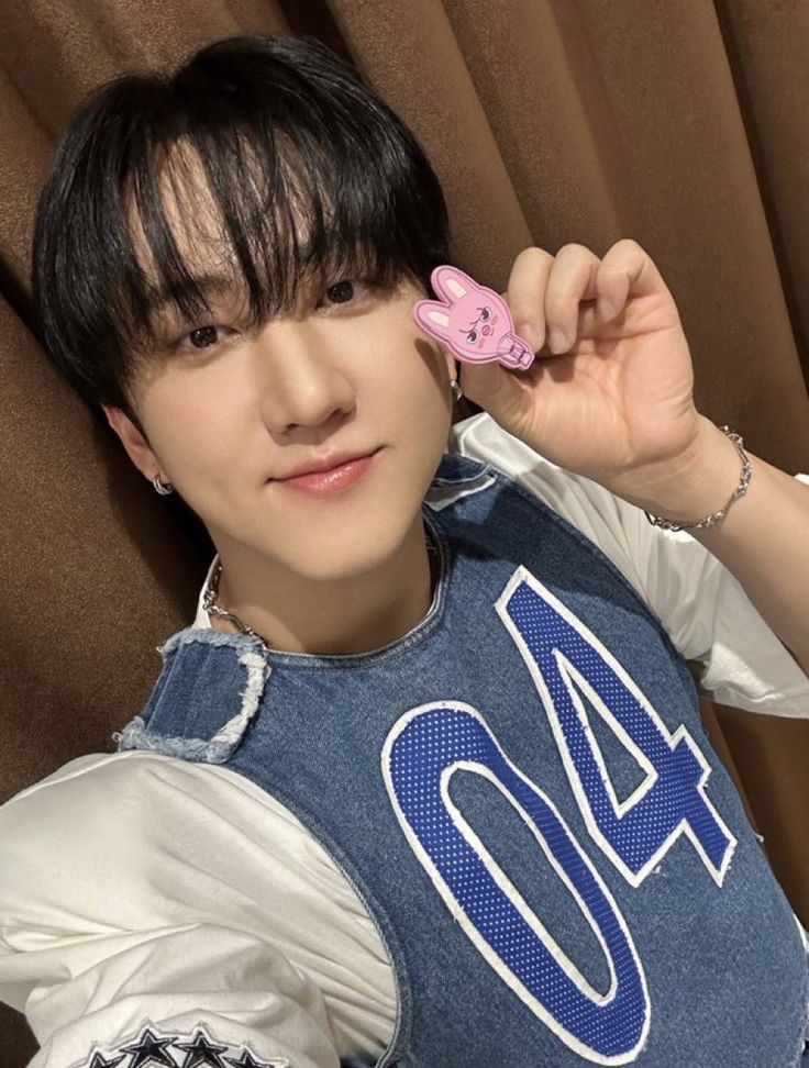 a young man holding a pink object in his right hand while wearing a denim vest