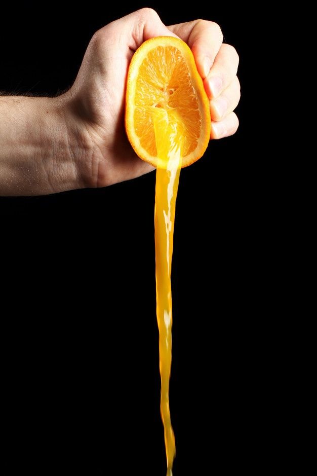 a hand holding an orange slice with juice pouring out of it to the other side