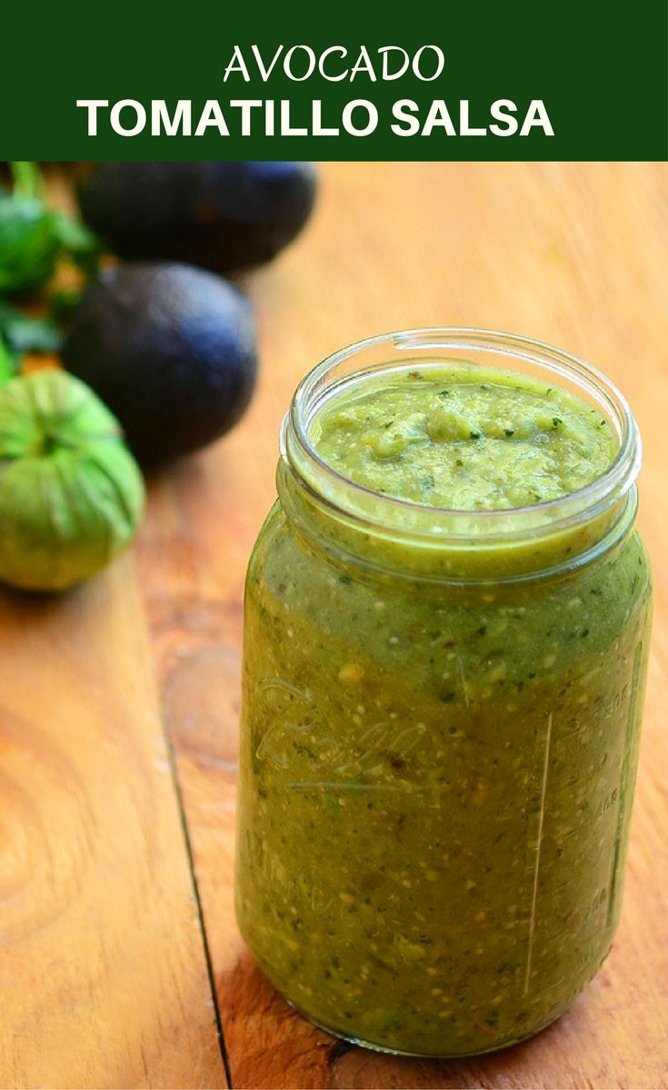 a green smoothie in a glass jar next to avocados on a wooden table