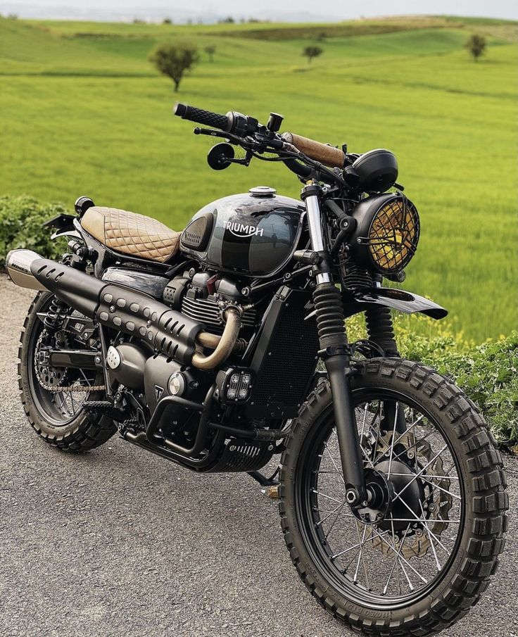 a motorcycle parked on the side of a road near a lush green field with trees