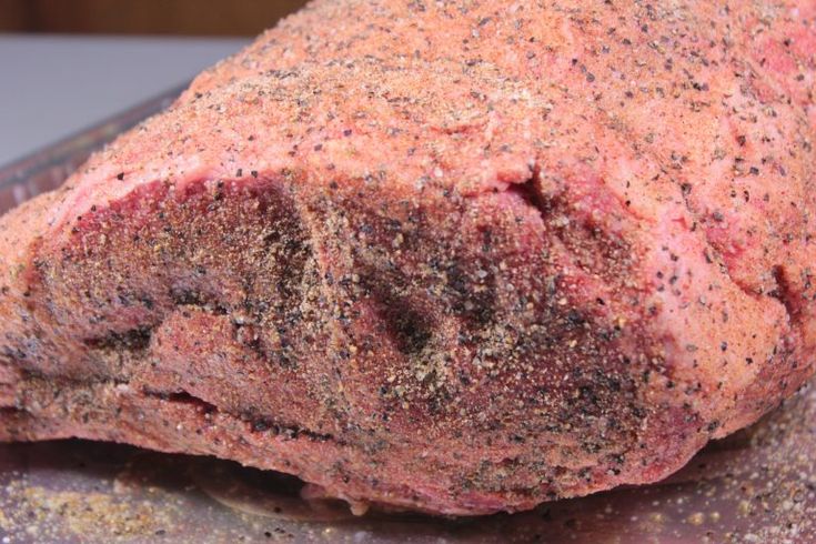 a large piece of meat sitting on top of a metal pan covered in seasoning