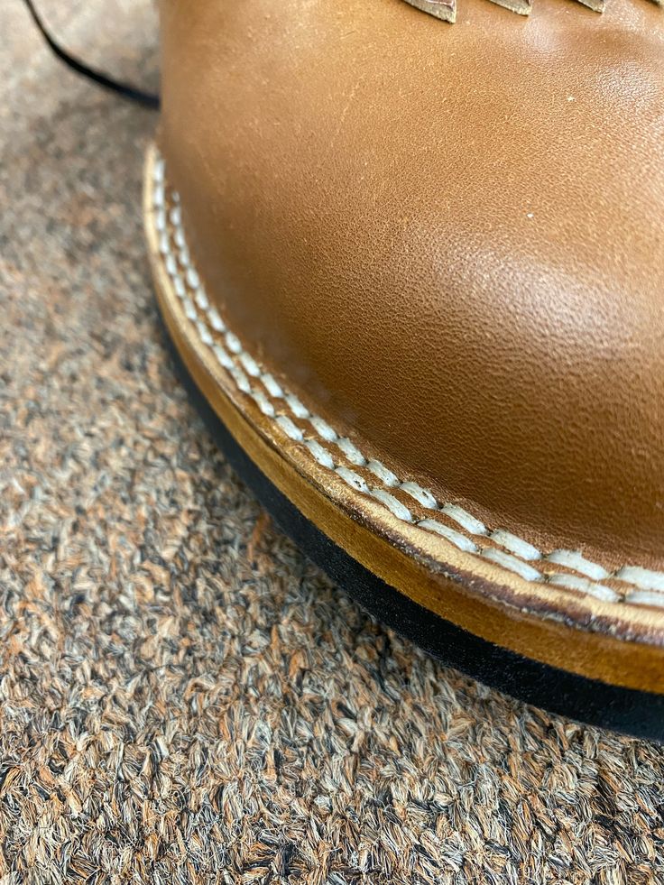 a brown shoe with white stitching on the bottom and side, sitting on carpet