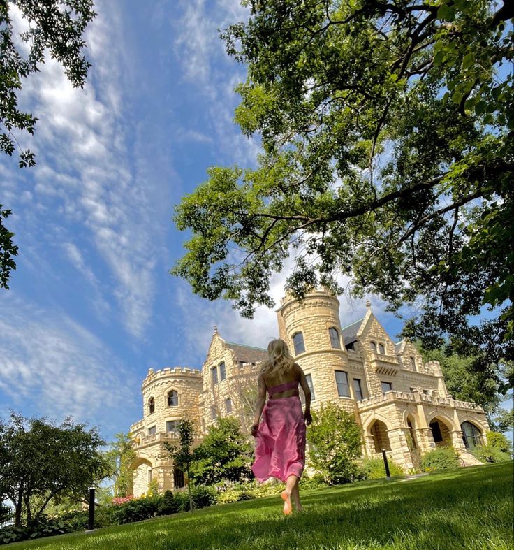 a woman in a pink dress is walking through the grass near a large castle like building