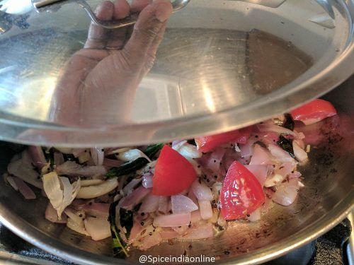 a pan with onions, tomatoes and other vegetables in it on top of a stove