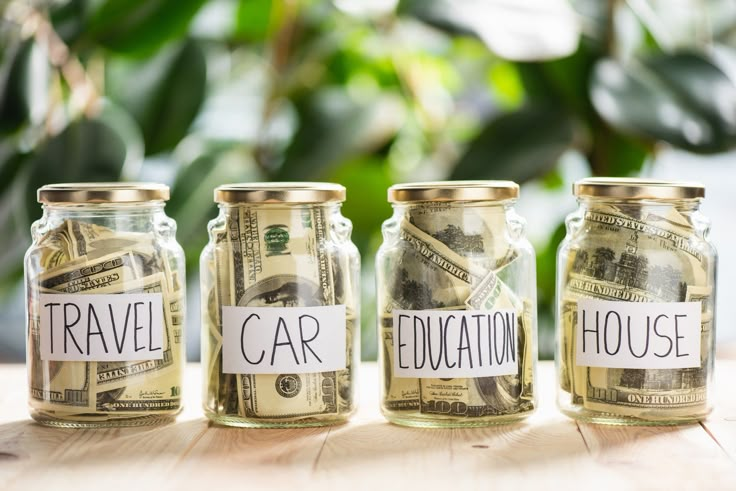 three glass jars filled with money labeled travel and car