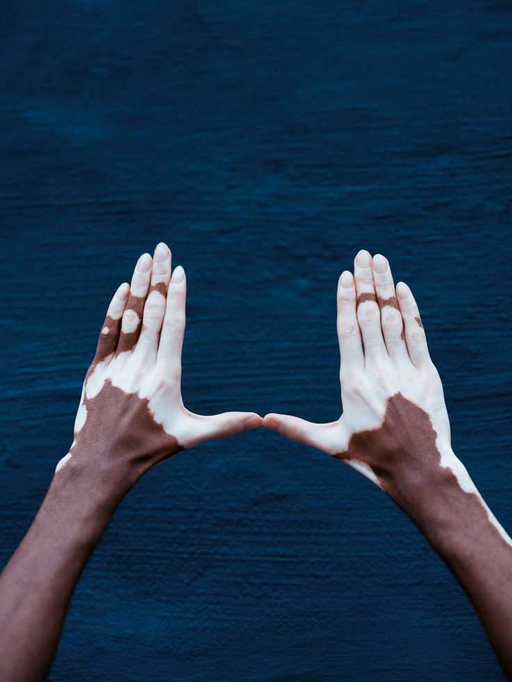 two hands reaching out towards each other with white and brown paint on their palms against a blue background