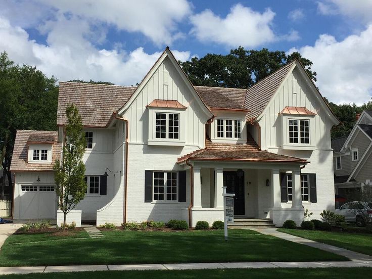 a white house with brown shingles on the roof and two story windows in front