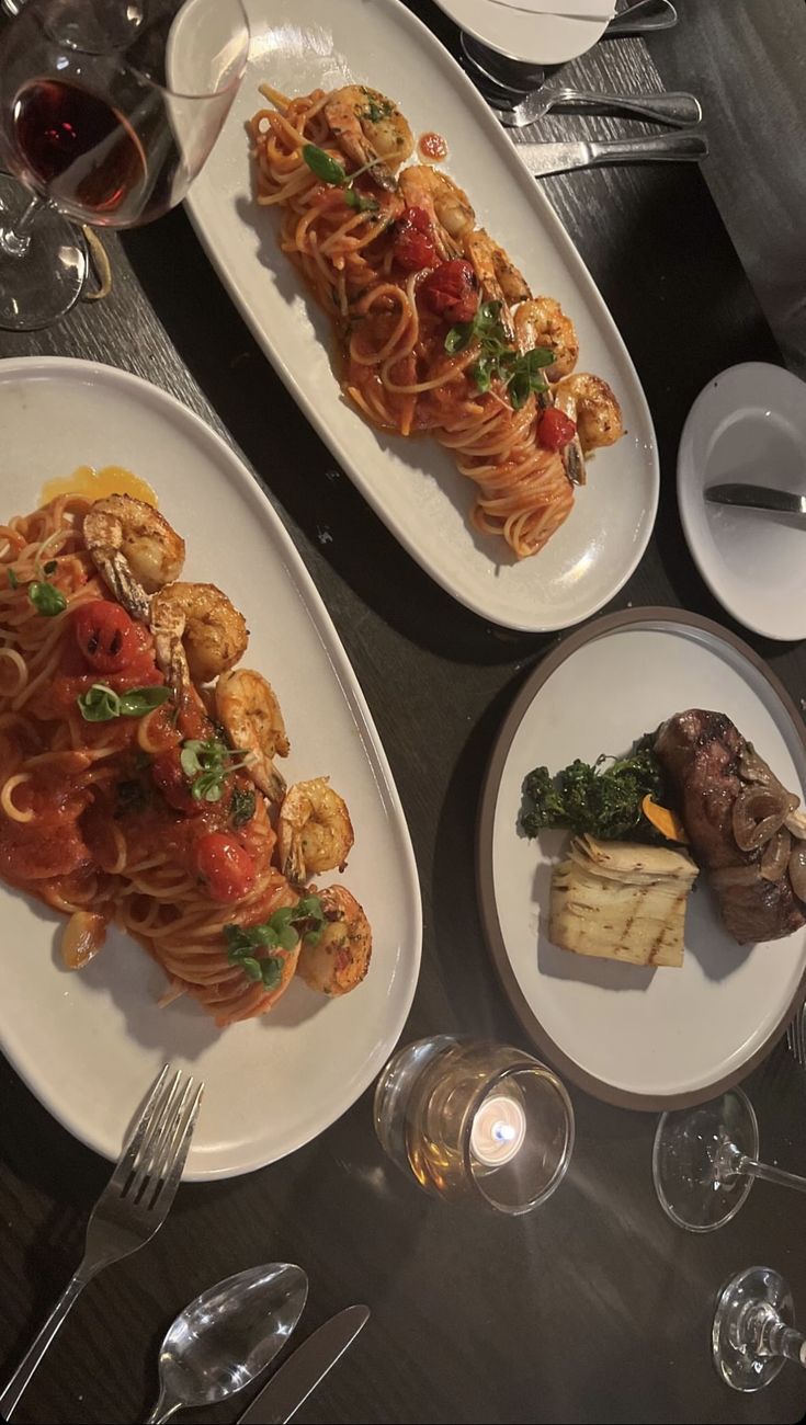 two white plates topped with pasta and veggies on top of a table next to wine glasses