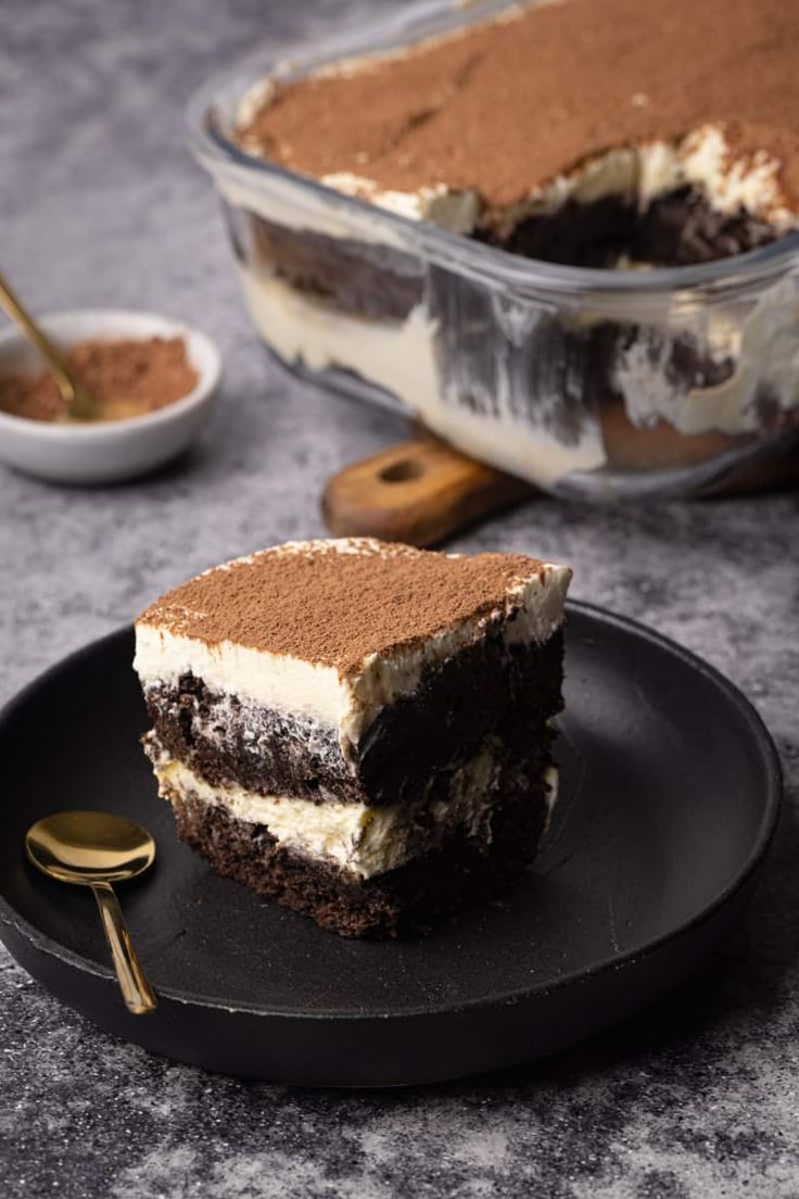 a piece of cake sitting on top of a black plate next to a fork and spoon