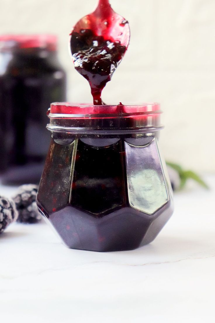 a spoon full of jam sitting on top of a table next to some blackberries