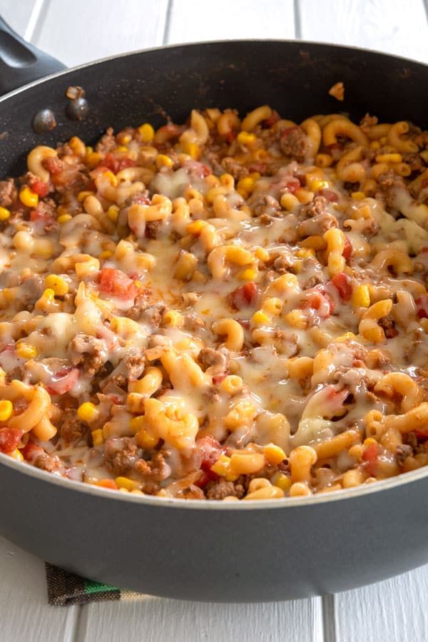 a skillet filled with macaroni and cheese on top of a wooden table