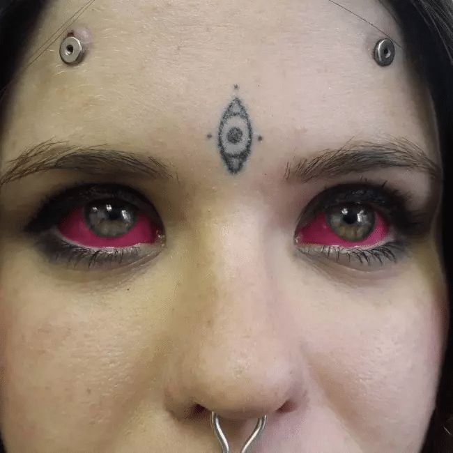 a close up of a person with red eyes and piercings on their nose, looking at the camera