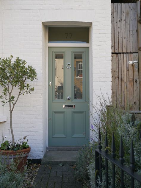 a green front door on a white brick building with potted plants and trees in the foreground