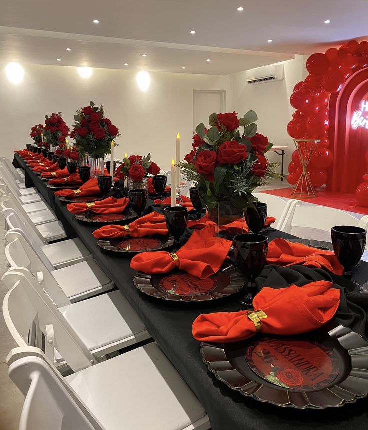 a long table set with red roses and black plates for formal dinner or party guests