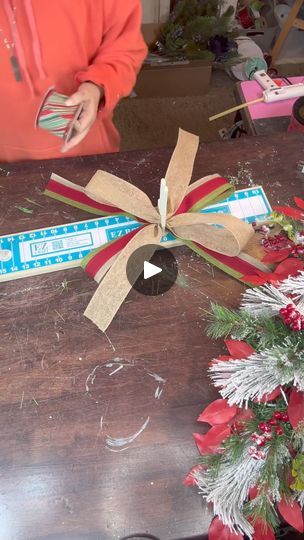 a woman is making a bow out of paper and ribbon on a wooden table with christmas decorations