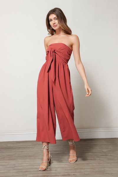 We're feeling sophisticated and sleek in this strapless jumpsuit. The Charlie Jumpsuit in Cinnamon is perfect for any and every upcoming event you may have. Pair this piece with strappy heels and a small handbag to complete the look.  Composition & Fit Strapless Tie Front Detail Gathered Waistline Pleated Leg Hem Spring Party Strapless Jumpsuit In Solid Color, Spring Strapless Jumpsuit For Evening, Strapless Jumpsuit For Spring Evening, Chic Strapless Jumpsuit For Night Out, Chic Strapless Jumpsuit For Going Out In Summer, Chic Strapless Jumpsuit For Party, Elegant Strapless Jumpsuit For Spring Outings, Elegant Strapless Jumpsuit For Spring Going Out, Spring Strapless Jumpsuit For Night Out