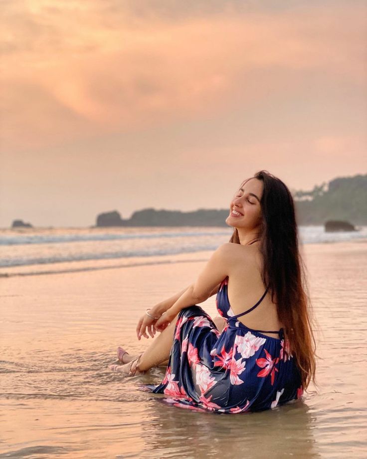 a woman is sitting in the water at the beach and looking up to the sky