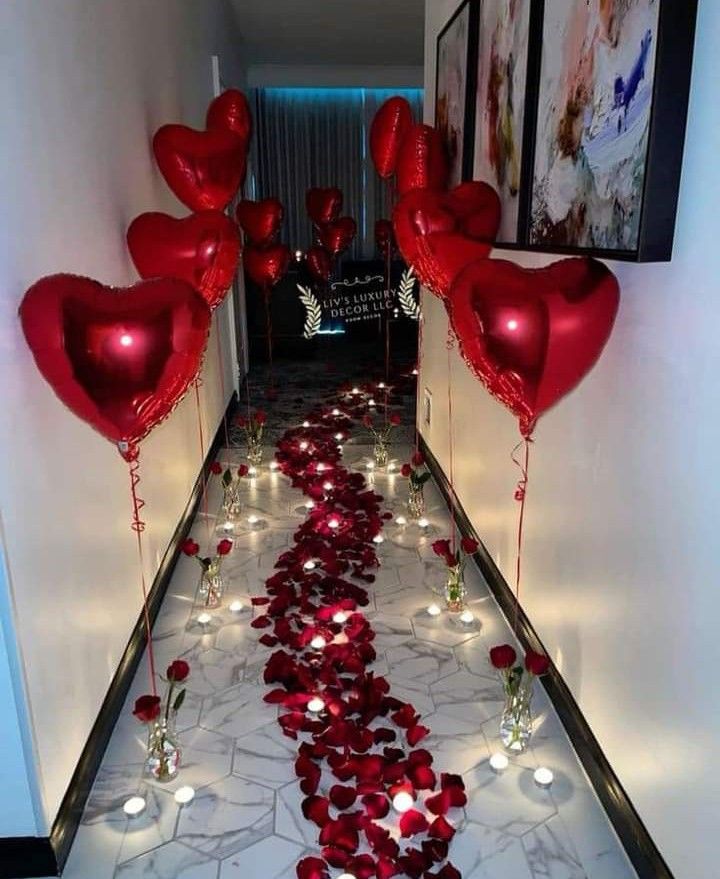 some red heart shaped balloons are on the floor in front of a hallway that is decorated with candles and flowers