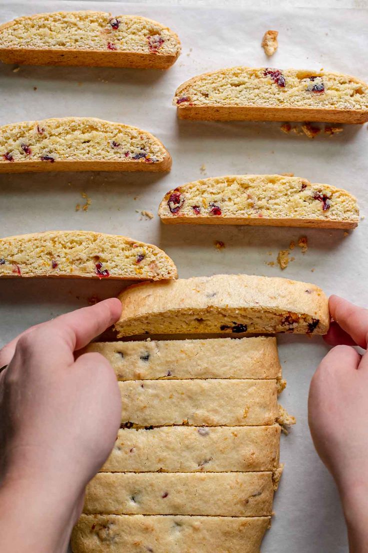 a person holding a piece of bread with cranberry toppings on it next to other pieces of bread