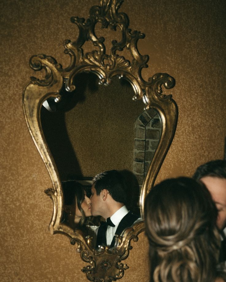 a man and woman are kissing in front of a golden mirror with gold trimming