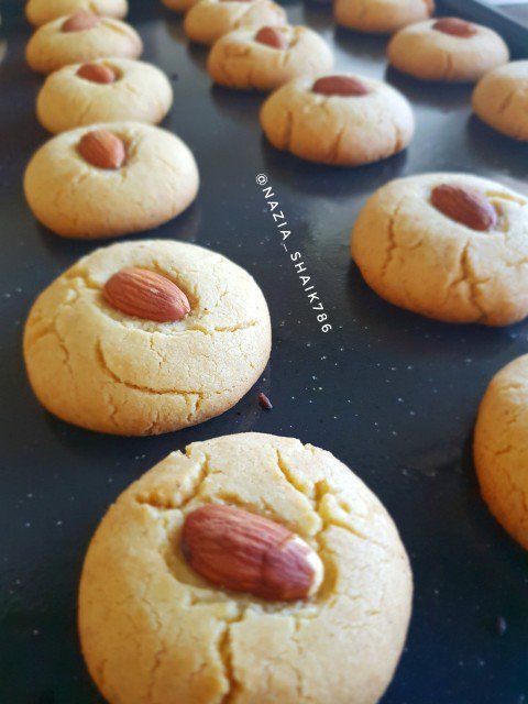 cookies with almonds are lined up in rows on a baking tray, ready to be baked