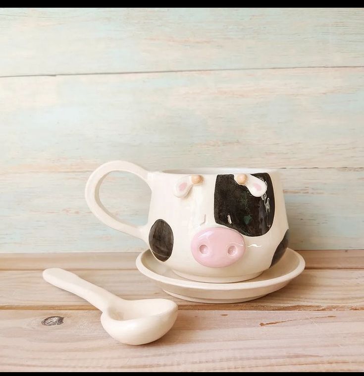 a cow mug and spoon sitting on top of a wooden table