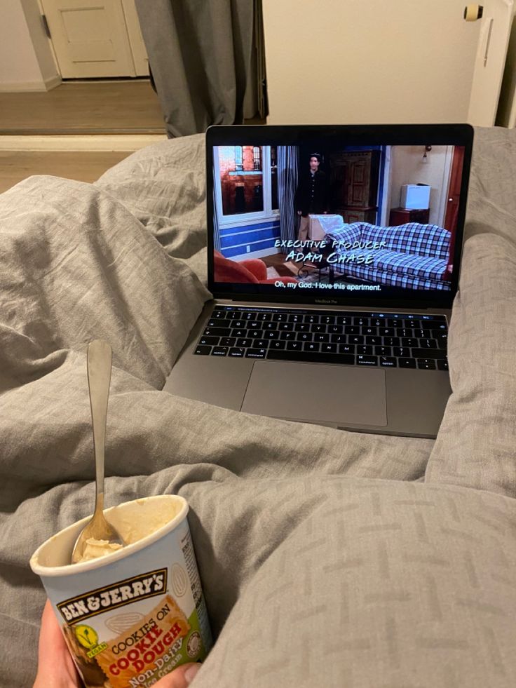 someone is watching tv on their laptop while eating ice cream from a cup in bed