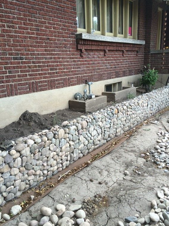 a stone wall next to a brick building with plants growing out of it and some dirt on the ground