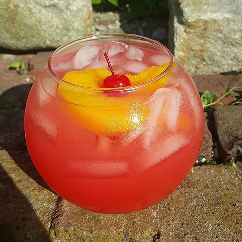 a drink in a glass with ice and cherries on the rim sitting on a rock