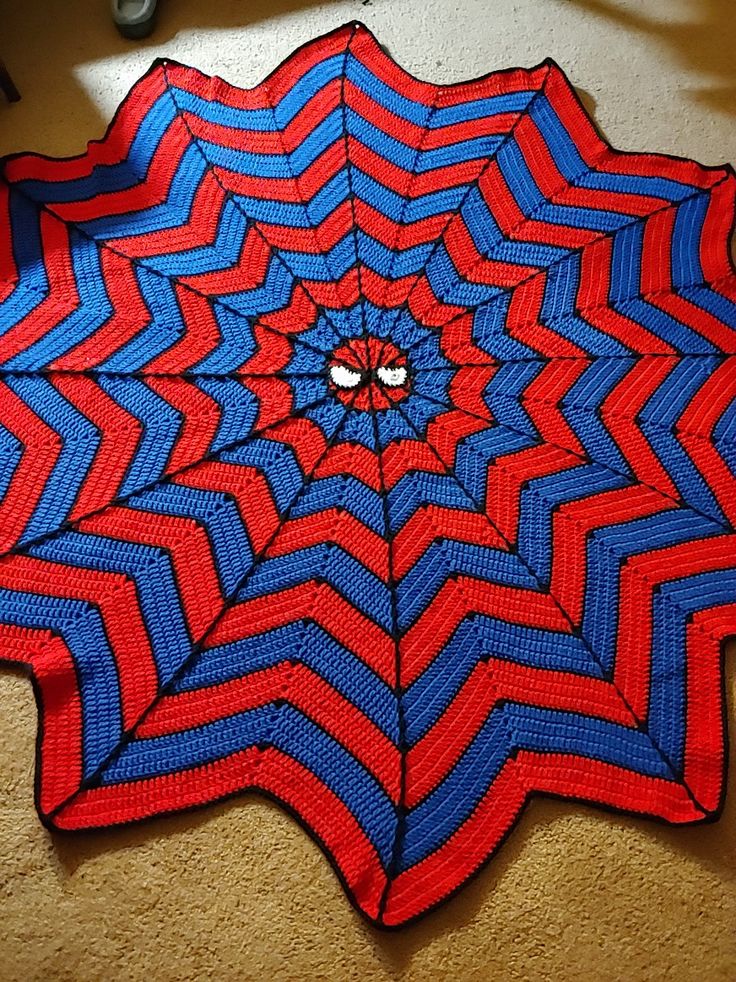 a red, blue and black knitted spider web with eyes on it's center