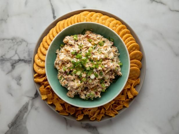 a bowl filled with chicken salad surrounded by crackers on a marble counter top,