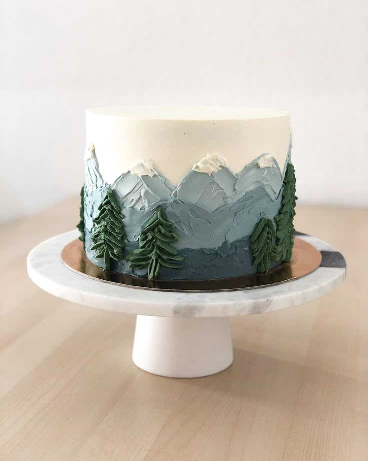 a cake with frosting and trees on top is sitting on a white plate that sits on a wooden table