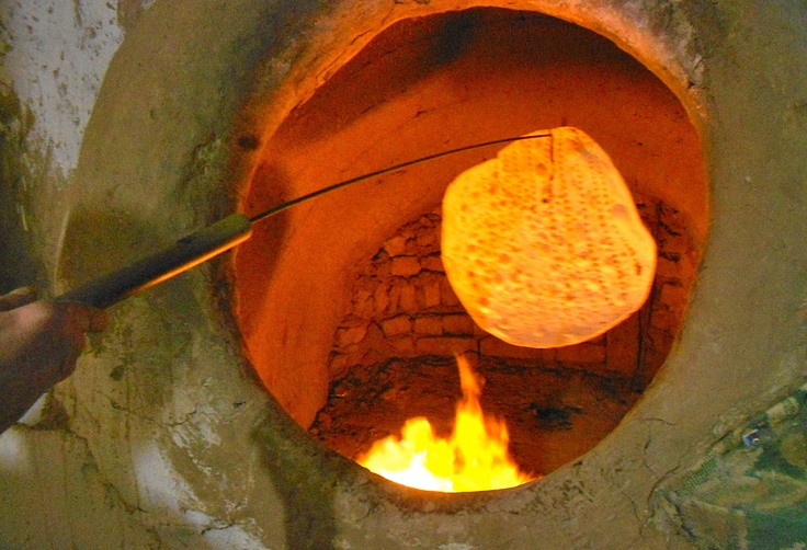 a person holding a spatula over a fire in a stone oven with flames coming from it