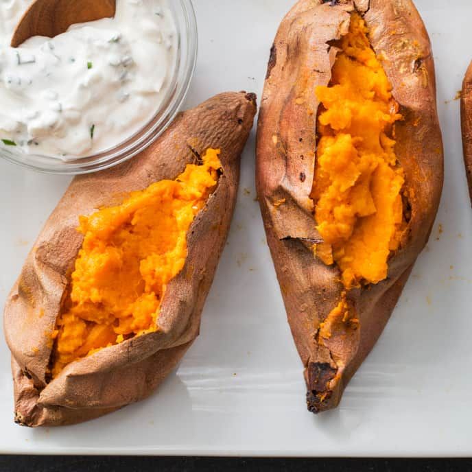 three baked sweet potatoes on a cutting board with dip