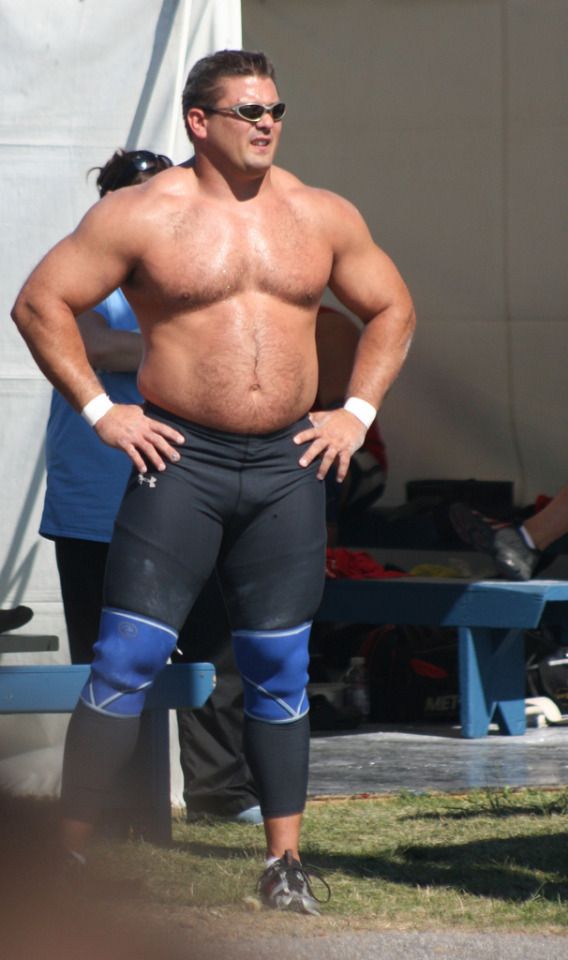 a man with no shirt on standing in front of a tent and wearing knee pads