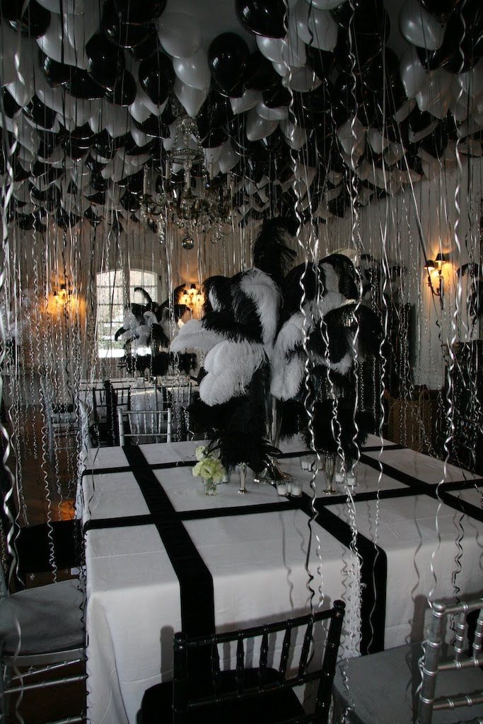 black and white balloons are hanging from the ceiling above a dining room table set for a party