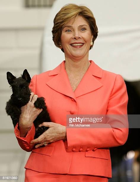 a woman in an orange suit holding a small black dog and smiling at the camera