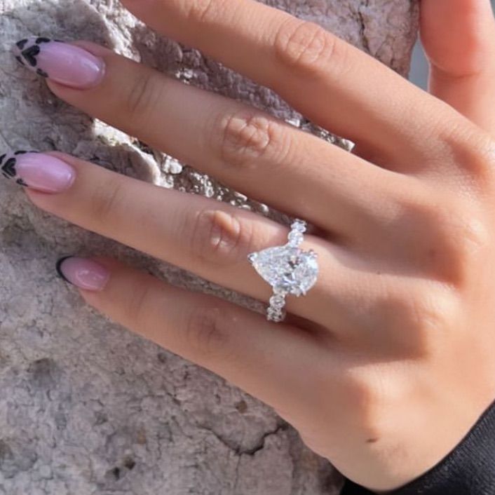 a woman's hand with a ring on top of her finger, next to a rock